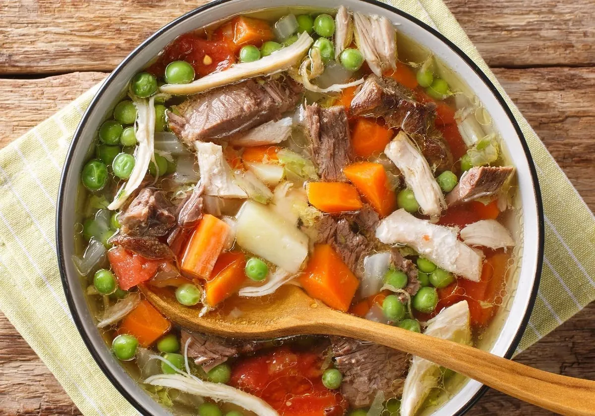 A pot of beef and vegetable soup with peas and carrots